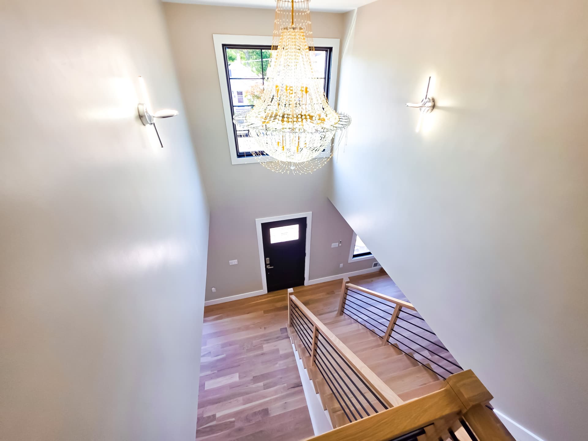 Two-story entry lobby with a crystal chandelier, open stair with wood and black metal railing and white oak floors